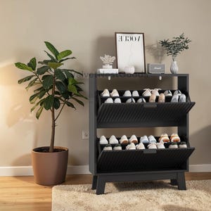 May include: A black shoe rack with two tilting compartments, each filled with various shoes. The rack is made of wood and has a minimalist design. A potted plant and decorative items are on the shelf above the shoe rack.