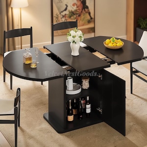 May include: A black, expandable dining table with a built-in storage cabinet. The table has a semi-circular design when extended, with a vase of white flowers and a bowl of lemons on the tabletop. The cabinet doors are open, revealing bottles and shelves.