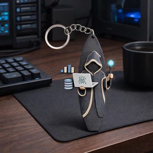 Op de afbeelding: Een zwarte en grijze sleutelhanger met een tovenaarachtig figuur dat een laptop en een gloeiende staf vasthoudt. Het figuur draagt een gewaad met capuchon en beige randen. De sleutelhanger bevat ook data-analyse-iconen en een zilveren ketting.