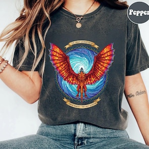 May include: Dark gray t-shirt featuring a vibrant graphic of a dragon with fiery red and orange wings, set against a swirling blue background. The text "THE GREAT LEONOPTERYX" and "TORUK MAKTO - THE LAST SHADOW" are displayed on banners.