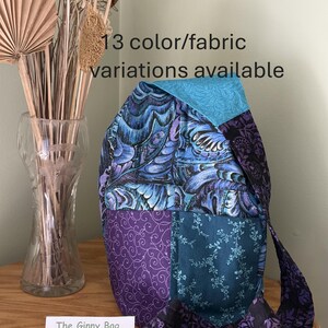 May include: A patchwork sling bag featuring various blue and purple fabric patterns, including floral and swirl designs. The bag has a wide shoulder strap and the text 13 color/fabric variations available is visible above the bag and on a small card.