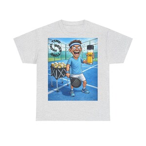 Puede incluir: Camiseta gris claro con una ilustración de dibujos animados de un jugador de tenis sosteniendo una cerveza y una raqueta. La imagen incluye el texto "PADEL TIME BEER TIME". El jugador está en una cancha de tenis azul.