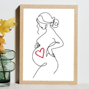 May include: A framed line art print featuring a pregnant person. The black line drawing depicts a side profile with a red heart on the abdomen. The artwork is set against a white background, framed in natural wood.
