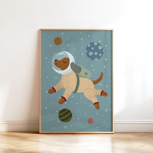 Op de afbeelding: Een ingelijste illustratie van een hond in een ruimtepak die in de ruimte zweeft. De hond is bruin met een beige ruimtepak, een heldere helm en rode accenten. Planeten van verschillende kleuren en maten zijn verspreid.