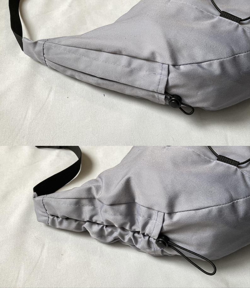 May include: A light gray crossbody bag with a black strap and drawstring closure. The bag is made of a smooth, possibly nylon, material. The bag has a rounded shape and a black drawstring closure.