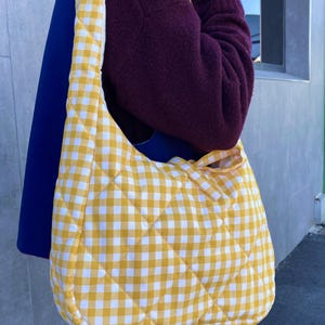 Pu&ograve; includere: Una borsa a tracolla trapuntata con motivo a quadretti gialli e bianchi. La borsa ha una forma arrotondata e una tracolla abbinata. La borsa &egrave; realizzata in un tessuto morbido e trapuntato. &Egrave; un accessorio elegante.