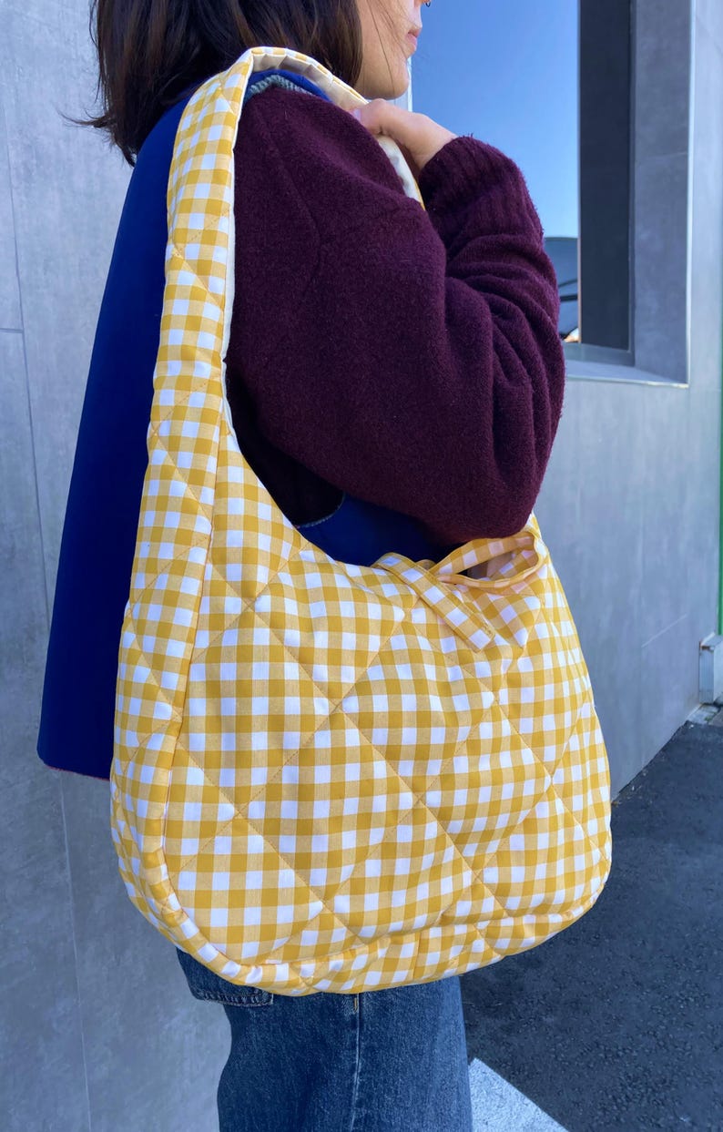 Pu&ograve; includere: Una borsa a tracolla trapuntata con motivo a quadretti gialli e bianchi. La borsa ha una forma arrotondata e una tracolla abbinata. La borsa &egrave; realizzata in un tessuto morbido e trapuntato. &Egrave; un accessorio elegante.
