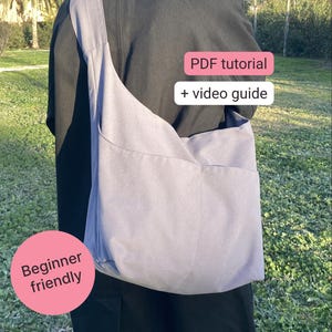 Op de afbeelding: Een lichtgrijze schoudertas met een grote zak wordt over de schouder gedragen. De tas is gemaakt van een zacht materiaal. Tekst op de afbeelding zegt "PDF tutorial + video guide" en "Beginner friendly".