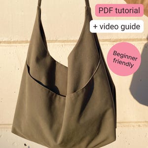 Könnte beinhalten: Eine olivgrüne Hobo-Tasche mit einem einzelnen Schulterriemen und einer geschwungenen Vordertasche. Das Bild enthält rosa Textfelder mit der Aufschrift: PDF tutorial, + video guide und Beginner friendly.