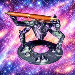May include: A brown wooden pen held horizontally by a dark, metallic-looking, multi-limbed creature figurine. The creature stands on a circular base featuring small pyramid-shaped structures and a central hole, set against a vibrant galaxy background.