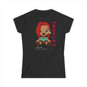 Puede incluir: Camiseta negra con un personaje de dibujos animados pixelado con pelo rojo, una parte superior turquesa y pantalones cortos marrones. El texto "[ROXIE]" está alineado verticalmente en el lado derecho. Debajo del personaje están las palabras "// REBEL SOUL PURE CHAOS. HIGH VOLUME. !"