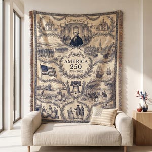 May include: A beige and navy blue tapestry with a historical illustration of the United States. The tapestry features images of George Washington, the American flag, and the text "AMERICA 250 1776-2026". The tapestry has a fringed edge and is displayed above a beige sofa.
