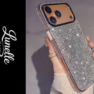 Puede incluir: Una funda de teléfono adornada con cristales brillantes, con un marco de oro rosa. La funda tiene una carcasa de cámara negra y la marca "Lunelle CASE Dreamy Phone Covers" es visible en el lado izquierdo.