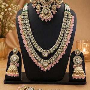 Könnte beinhalten: Ein aufwendiges, goldfarbenes Schmuckset mit Halsband, mehrreihiger Halskette, Ohrringen und Kopfschmuck. Das Set umfasst klare und rosa Edelsteine, grüne Akzente und kleine weiße Perlen. Der Schmuck wird auf einer schwarzen Schaufensterpuppe präsentiert.