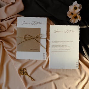 May include: Wedding invitation suite featuring two cards with torn edges. The cards have the names "Jessica & Batuhan" in elegant script. One card has a brown paper insert tied with twine. The date "27 05 23" is printed on both cards.