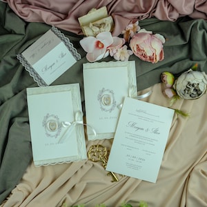 K&ouml;nnte beinhalten: Ein Set cremefarbener Hochzeitseinladungen mit verzierten ovalen Rahmen, Wachssiegeln und wei&szlig;en Satinb&auml;ndern. Die Karten zeigen die Namen Meryem & Ilker, das Datum 25.09.2026 und gedruckten Text. Enth&auml;lt k&uuml;nstliche rosa und wei&szlig;e Blumen.