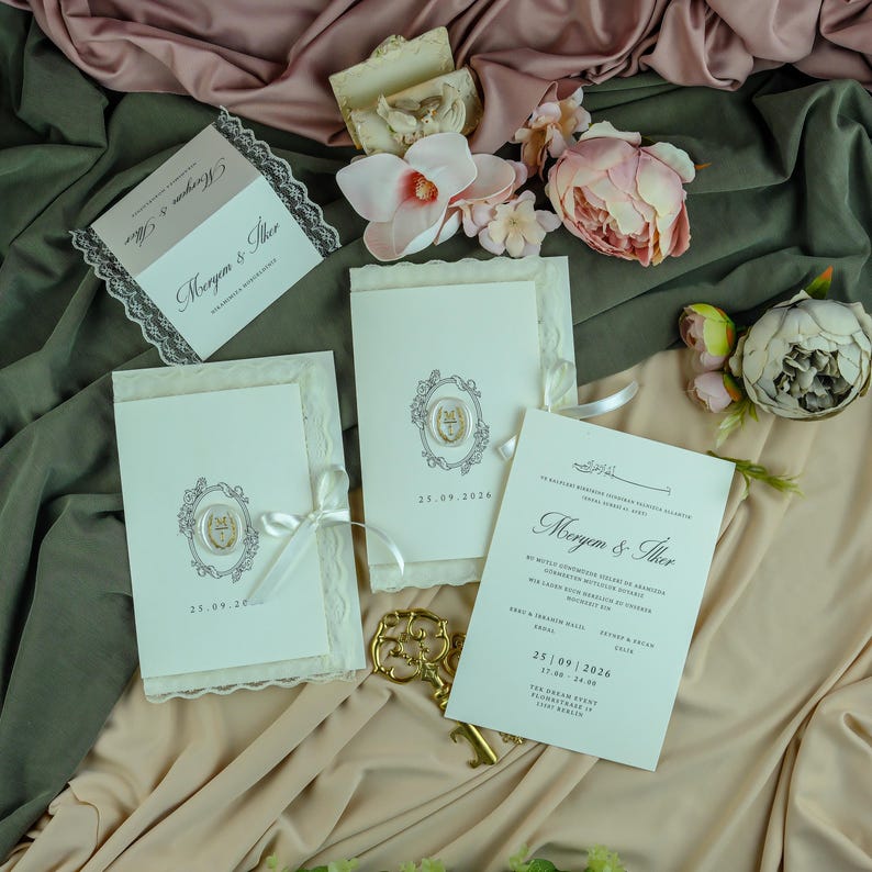 K&ouml;nnte beinhalten: Ein Set cremefarbener Hochzeitseinladungen mit verzierten ovalen Rahmen, Wachssiegeln und wei&szlig;en Satinb&auml;ndern. Die Karten zeigen die Namen Meryem & Ilker, das Datum 25.09.2026 und gedruckten Text. Enth&auml;lt k&uuml;nstliche rosa und wei&szlig;e Blumen.