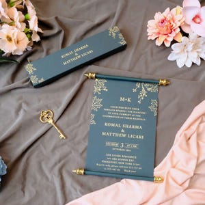 Peut inclure: Un faire-part de mariage en forme de parchemin bleu sarcelle foncé avec des motifs de feuilles dorées et le texte mentionnant Komal Sharma et Matthew Licari, accompagné d'une boîte rectangulaire assortie et d'une clé squelette dorée.