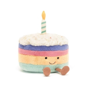 Peut inclure: Un gâteau en peluche multicolore avec un visage souriant et de petits pieds bruns. Une bougie rayée avec une flamme jaune est posée dessus. Le gâteau est un jouet doux pour enfants.