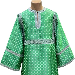 May include: A green tunic with white cross patterns and decorative trim. The long-sleeved garment features a keyhole neckline and is displayed on a mannequin. The trim includes circular and cross designs.