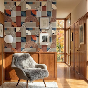 May include: A mid-century modern interior featuring a patterned wallpaper in shades of brown, beige, and navy blue. A gray armchair with a faux fur throw sits on a white rug. The room has wooden paneling and a hallway with large windows.
