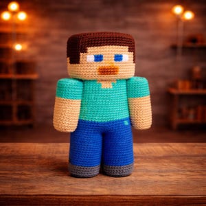 May include: A handmade crochet figure of a Minecraft character, featuring a blocky head with brown hair, blue eyes, and a tan face. The figure wears a teal shirt, blue pants, and has tan arms. The figure is approximately 8 inches tall.