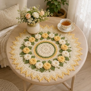 May include: A round crochet doily featuring a central cream-colored lace pattern surrounded by a wreath of three-dimensional yellow and white crocheted roses and green leaves, finished with a pointed, scalloped edge in cream and yellow yarn.