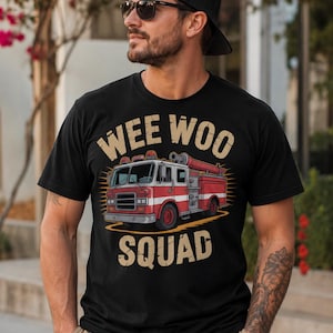 Pode incluir: Camiseta preta com um gráfico de um caminhão de bombeiros vermelho e branco e as palavras "WEE WOO SQUAD" em uma fonte desgastada. A camiseta é de manga curta e tem gola redonda.