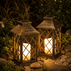 May include: Two antique-style solar lanterns with a diamond lattice design. The lanterns have a warm, golden finish and a handle for hanging. Each lantern contains a glowing, white candle-like light, perfect for outdoor decor.