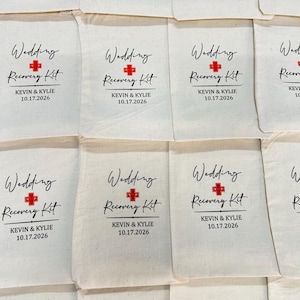 Puede incluir: Bolsas de tela color crema con la inscripci&oacute;n "Wedding Recovery Kit" en escritura negra, un s&iacute;mbolo de cruz roja y los nombres "KEVIN & KYLIE" con la fecha "10.17.2026". Se ven varias bolsas.