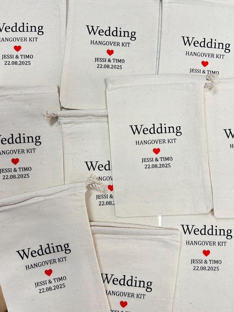 Puede incluir: Varios bolsos de tela blanquecina con cordones. Cada bolso tiene impreso en negro las palabras "Wedding HANGOVER KIT", un coraz&oacute;n rojo y los nombres "JESSI & TIMO" con la fecha "22.08.2025".