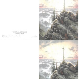 May include: A landscape print depicting a cross on a rocky mountain, set against a sunrise or sunset. The artwork is signed "THOMAS KINKADE Painter of Light". The print is a religious themed artwork.