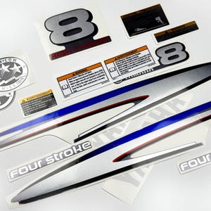 May include: A collection of various stickers and decals, including a large silver number 8 with "HIGH THRUST" text, and long, silver decals with blue and red stripes. Other stickers include "ULTRA-LOW EMISSION" and "FOUR STROKE".
