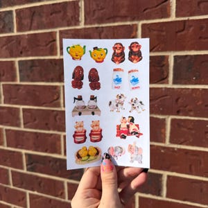 May include: A sheet of stickers featuring various vintage-style figurines. The stickers include teapots, monkeys, salt and pepper shakers, dogs, bears, a couple on a bench, ducklings, and elephants. The stickers are in various colors.