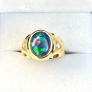 Könnte beinhalten: Ein goldener Ring mit einem ovalen schwarzen Opal-Edelstein. Der Opal zeigt ein lebendiges Farbspiel mit Grün-, Blau- und Rottönen. Der Ring hat kleine Diamantakzente und ist in einem goldenen Band gefasst.