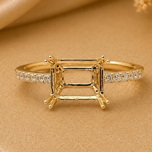 May include: A gold ring setting featuring a rectangular prong mount designed to hold a centre stone. The band is accented with a row of small, clear pavé-set stones along the top half, creating a refined and polished appearance for jewellery.