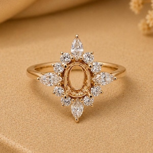 May include: A gold ring featuring a central oval-shaped empty setting surrounded by a halo of marquise and round-cut clear stones arranged in a starburst pattern. The band is thin and polished gold, with the text ElinaRoseCo visible below.