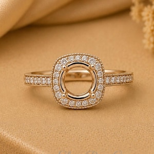 Peut inclure: Une bague en or rose dotée d'un sertissage halo de forme carrée avec une monture centrale vide. Le halo et l'anneau sont incrustés de petites pierres rondes transparentes. Le métal a une finition polie et l'anneau présente un détail milgrain.