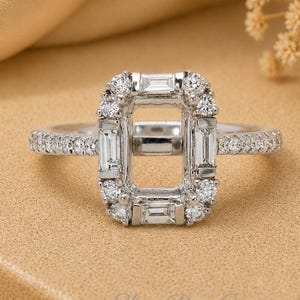 May include: A silver-toned ring featuring a rectangular centre setting framed by a combination of baguette-cut and round-cut stones. The band is adorned with small round stones along the sides, creating a detailed and symmetrical design.