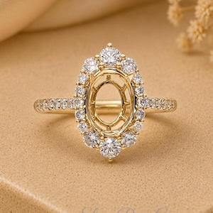 May include: A gold ring setting featuring an oval-shaped centre mount surrounded by a halo of small round clear stones. The band is also adorned with a row of small round clear stones along the sides. The text ElinaRoseCo is visible.