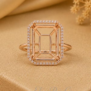 May include: A rose gold ring setting featuring a rectangular head designed for a center stone. The rectangular frame is bordered by a halo of small, clear, round-cut stones. The band is thin and smooth, connecting to the base of the setting.