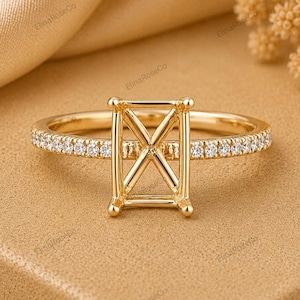 May include: A gold ring featuring a rectangular setting with an X-shaped metal support structure in the center. The band is thin and adorned with a row of small, clear, round-cut stones along the top half of the shank, set in polished gold.