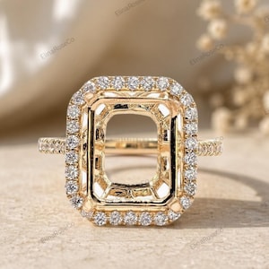 May include: A gold ring setting with a rectangular center and a halo of small, round diamonds. The band is also adorned with small diamonds. The ring is set against a neutral background.
