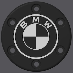 Könnte beinhalten: Schwarzes kreisförmiges Emblem mit dem BMW-Logo in Weiß. Das Logo ist ein weißer Kreis mit den Buchstaben "BMW" darum und einem geteilten inneren Kreis in Schwarz und Weiß. Das Emblem hat sechs gleichmäßig verteilte Löcher.