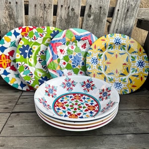 May include: A set of four round plates and a stack of four bowls featuring vibrant, multi-colored geometric and floral patterns. The plates display distinct designs in red, green, turquoise, and yellow, while the bowls feature a white base.