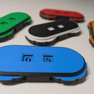 May include: A selection of multi-coloured 3D-printed number counters. The counters are in blue, green, red, black, and orange. Each counter has a digital display showing the number 09.