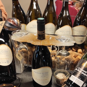 Peut inclure: Plusieurs bouteilles de vin avec des étiquettes variées, dont "Pouilly-Fuisse" et "Saint-Veran". Un plateau de service décoratif supporte des verres à vin et un bouchon. Les bouteilles sont disposées sur une table avec une guirlande lumineuse.