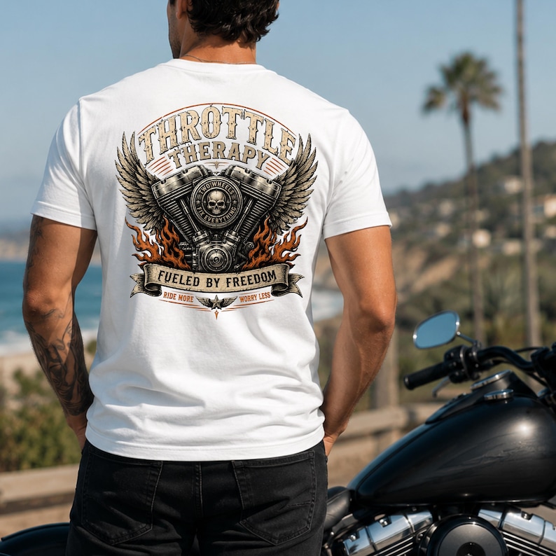 May include: A white t-shirt featuring a graphic on the back with a motorcycle engine, wings, and flames. The text reads THROTTLE THERAPY, FUELED BY FREEDOM, TWO WHEELS FIX EVERYTHING, and RIDE MORE WORRY LESS, centered around a skull illustration.