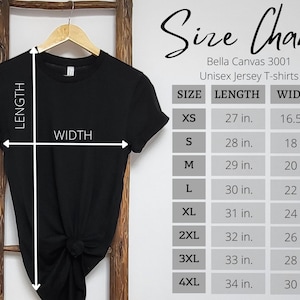 May include: A black t-shirt hanging on a wooden hanger with a size chart for Bella Canvas 3001 unisex jersey t-shirts. The chart lists lengths and widths in inches for sizes XS through 4XL, with white arrows indicating how to measure the garment.