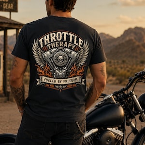 May include: A charcoal gray t-shirt featuring a back graphic of a motorcycle engine with wings, flames, and a skull. The text reads Throttle Therapy, Fueled By Freedom, Two Wheels Fix Everything, and Ride More Worry Less in a vintage style font.